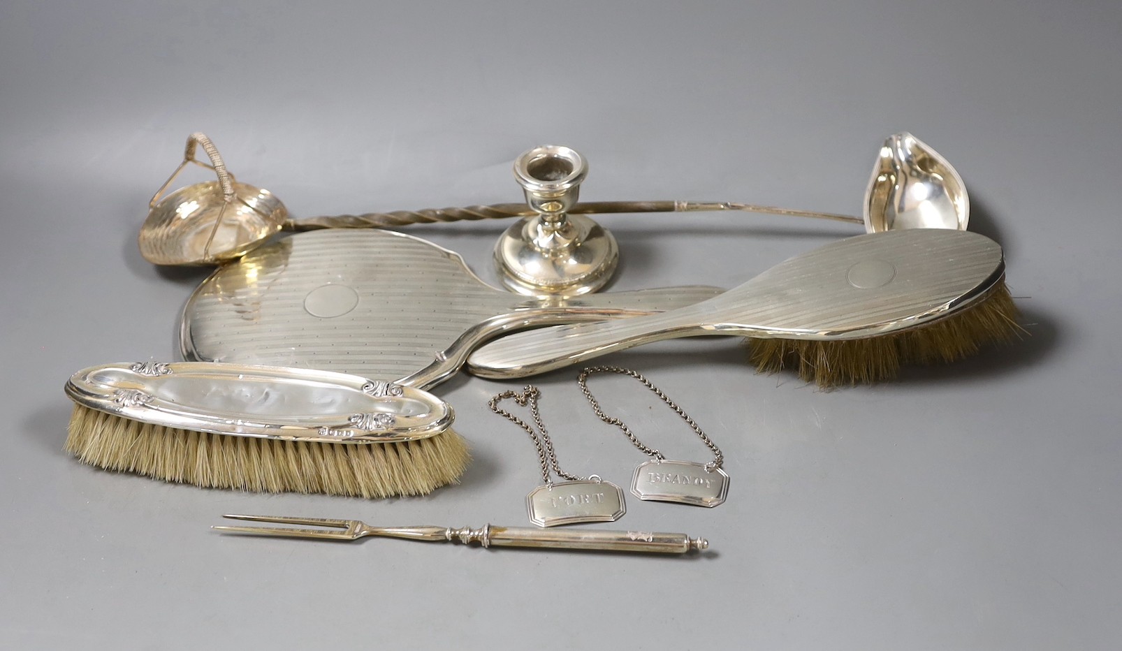 A silver mounted hand mirror and two brushes, and 800 toasting fork?, a dwarf candlestick, white metal toddy ladle(a.f.), 925 bonbon basket and a pair of late Victorian wine labels by George Unite.